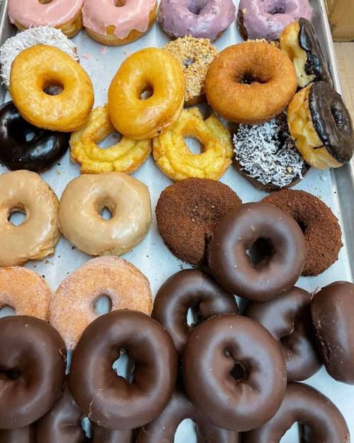 A variety of colorful donuts arranged on a tray, including glazed, chocolate, and sprinkled options.