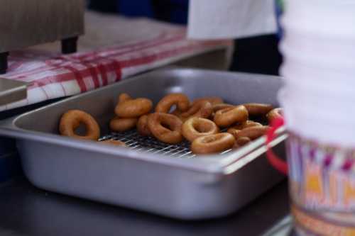 A tray of freshly fried donuts resting on a wire rack, with a checkered cloth in the background.