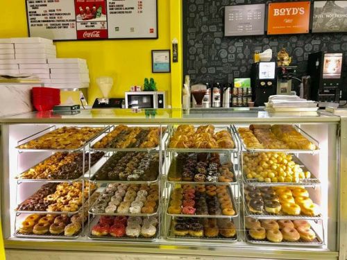 A display case filled with a variety of colorful donuts and pastries, set against a bright yellow wall.