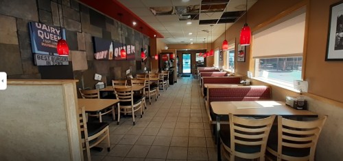 Interior of a restaurant with booths and tables, red pendant lights, and a view of the entrance.
