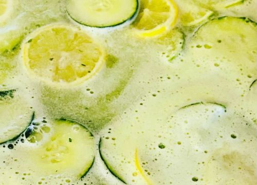 Close-up of a refreshing drink with slices of lemon and cucumber floating in a bubbly, greenish liquid.