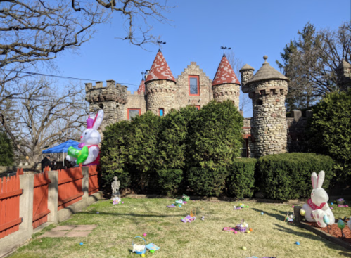 A stone castle with red turrets, surrounded by greenery and decorated with Easter bunnies and colorful eggs on the lawn.