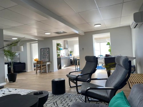 A modern living space featuring two armchairs, a coffee table, and an open kitchen area with natural light.
