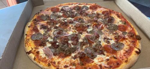A large pizza topped with pepperoni, sausage, ham, and cheese in a cardboard box.