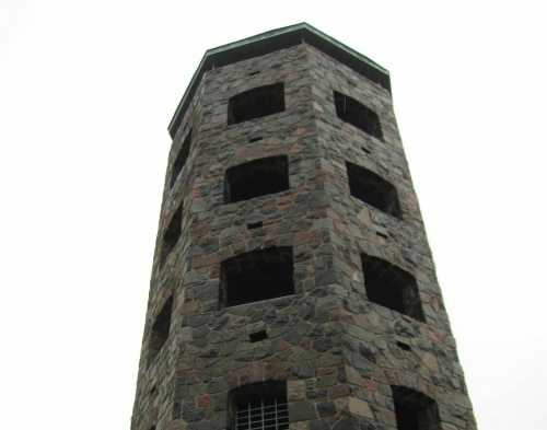 A tall stone tower with multiple windows and a gated entrance, set against a gray sky.