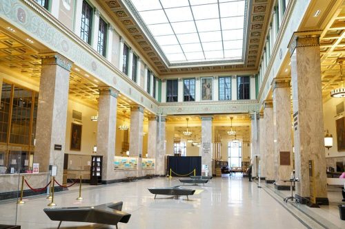 Interior of a grand hall with tall columns, large windows, and elegant lighting, featuring a spacious, open layout.