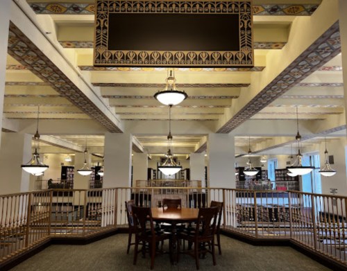 A spacious interior with elegant lighting, featuring a wooden table surrounded by chairs and decorative ceiling details.