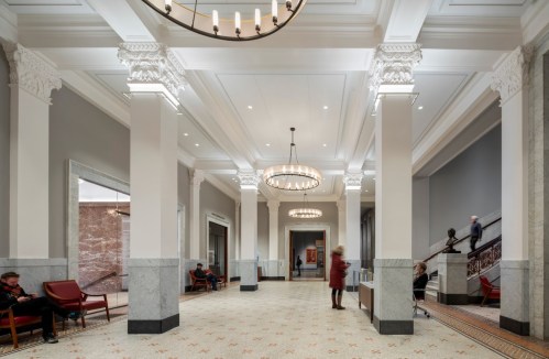 A spacious, elegant lobby with high ceilings, chandeliers, and marble columns, featuring seating areas and artwork.