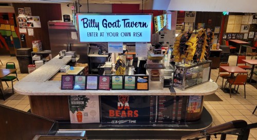 A view of the Billy Goat Tavern counter with a menu, drinks, and a sign reading "Enter at Your Own Risk."