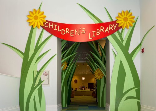Colorful entrance to a children's library, featuring a red banner and green grass-like decorations with sunflowers.