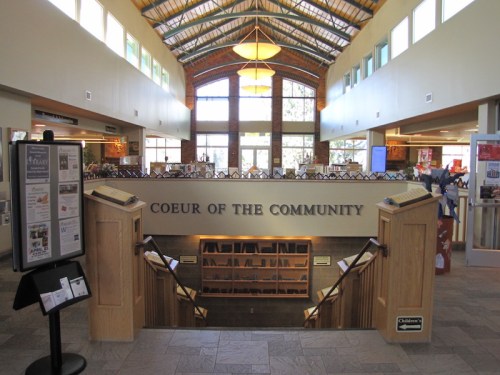 Interior view of a community center with a high ceiling, wooden beams, and a staircase leading to a lower level.