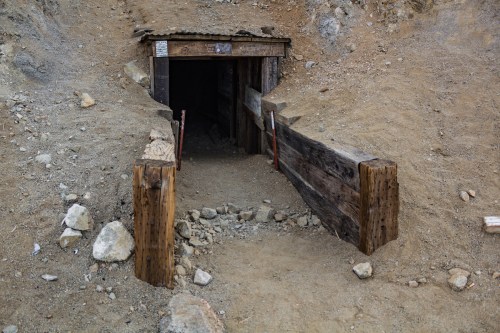 Entrance to a rustic mine tunnel, framed with wooden beams and surrounded by rocky terrain.