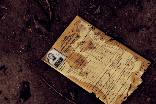 A weathered document with a photo, lying on a dirt surface, showing signs of age and neglect.