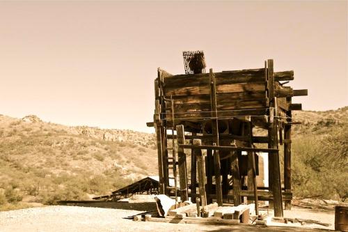 Abandoned wooden structure in a desert landscape, surrounded by hills under a clear sky.