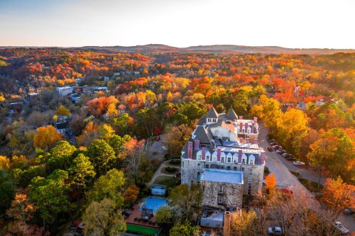 Aerial view of a castle surrounded by vibrant autumn foliage and rolling hills at sunset.