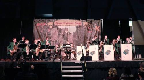 A jazz band performs on stage, featuring musicians with instruments and a backdrop of a cityscape.
