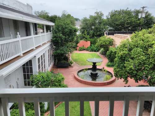 View from a balcony overlooking a lush courtyard with a fountain, greenery, and brick pathways.