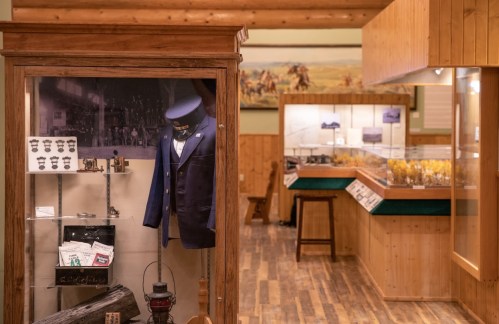 A display case with a vintage suit and artifacts in a wooden museum interior, showcasing historical items.