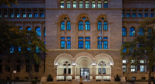 Historic building facade at night, featuring arched windows and decorative stonework, illuminated softly.