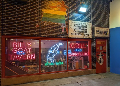 Neon sign for Billy Goat Tavern featuring "Grill and Carry Outs," with a goat logo and a "Born 1934" date.