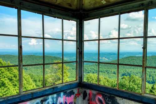 View from an observation tower with large windows overlooking green mountains and a blue sky with clouds.