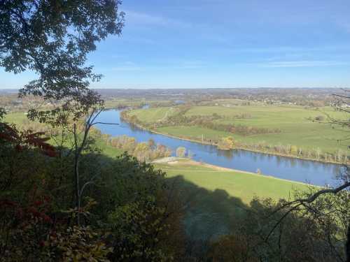 A scenic view of a winding river surrounded by lush green fields and trees under a clear blue sky.