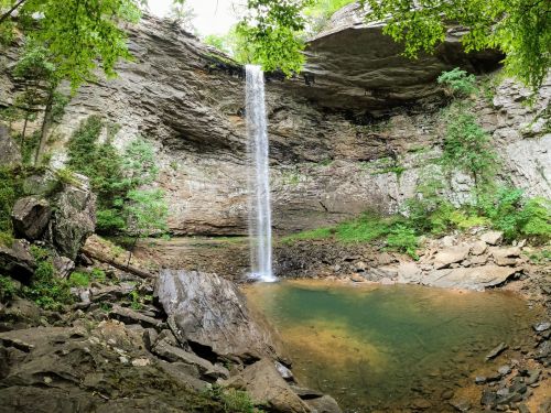 A serene waterfall cascades into a clear pool, surrounded by rocky cliffs and lush greenery.
