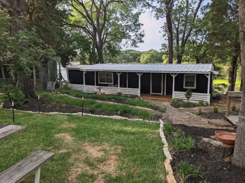 A cozy, dark blue cabin with a metal roof, surrounded by greenery and trees, set in a peaceful outdoor area.