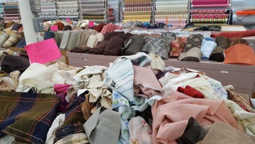 A colorful assortment of fabric rolls and scraps piled on tables in a fabric store.