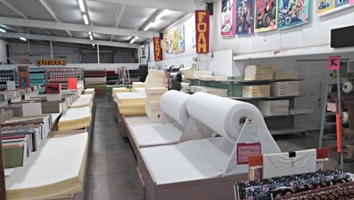 A fabric store interior with rolls of fabric, foam sheets, and shelves filled with colorful materials.