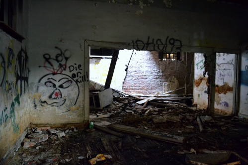 An abandoned room with graffiti on the walls and debris scattered on the floor, illuminated by a beam of light.