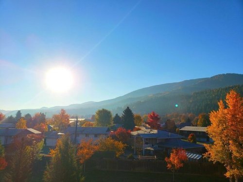 A vibrant autumn landscape with colorful trees, houses, and a bright sun shining over distant mountains.