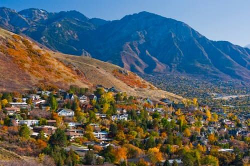 A scenic view of a hillside neighborhood surrounded by mountains, showcasing vibrant autumn foliage.
