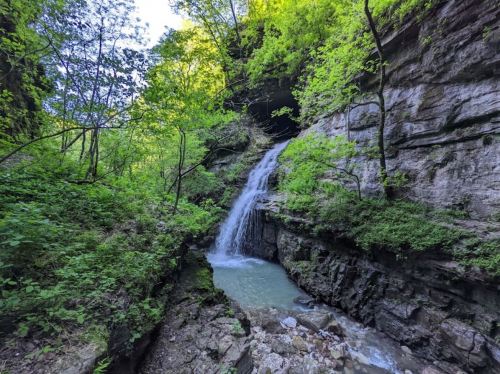 A serene waterfall cascades down rocky cliffs, surrounded by lush green foliage and a tranquil pool below.