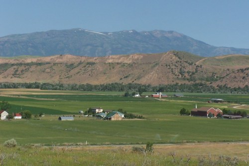 A scenic view of green fields and farms with mountains in the background under a clear blue sky.