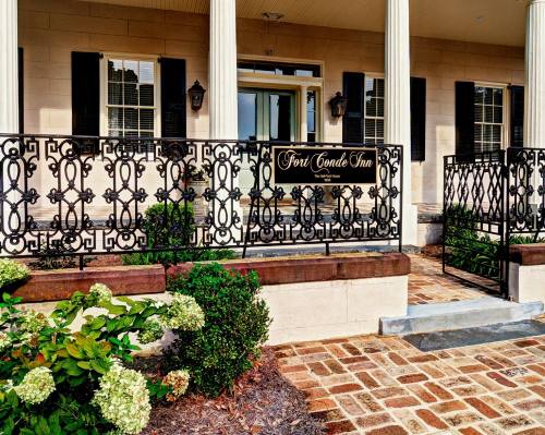 Front entrance of Fort Conde Inn featuring a decorative iron railing and lush greenery.