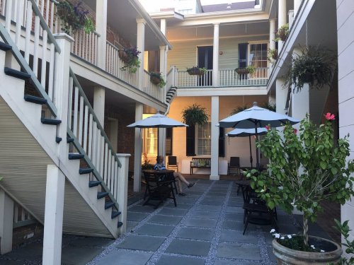 A serene courtyard with stairs, umbrellas, and potted plants, featuring seating areas and a warm, inviting atmosphere.