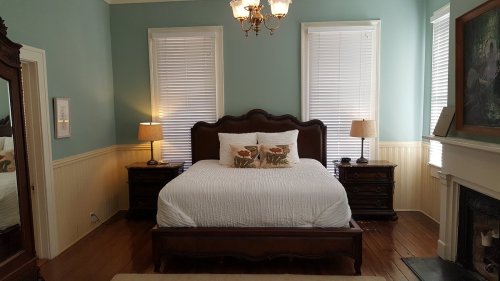Cozy bedroom with a wooden bed, two lamps, and a mirror, featuring light blue walls and hardwood floors.