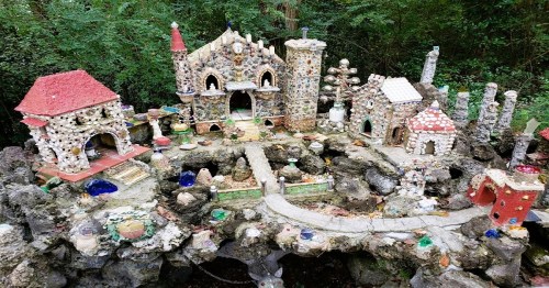 A whimsical miniature village made of colorful stones and shells, surrounded by greenery.