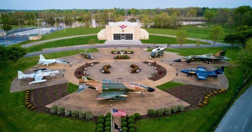 Aerial view of a military aircraft display with various planes arranged around a central monument in a park setting.