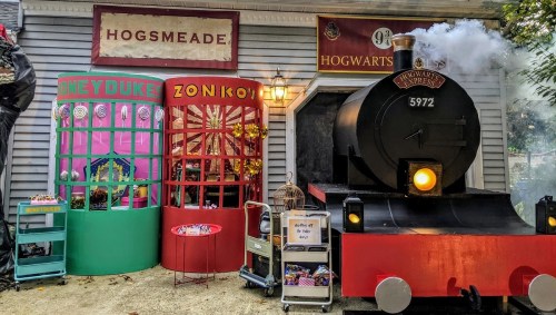 A whimsical storefront in Hogsmeade with colorful shops and a steam train, evoking a magical atmosphere.