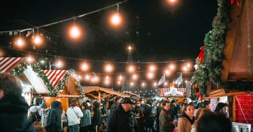 A bustling night market decorated with festive lights and holiday decorations, filled with people enjoying the atmosphere.