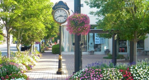 A charming street in Fairhope with a clock, colorful flower beds, and trees lining the sidewalk.