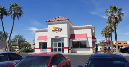Exterior of an In-N-Out Burger restaurant with palm trees and a clear blue sky.