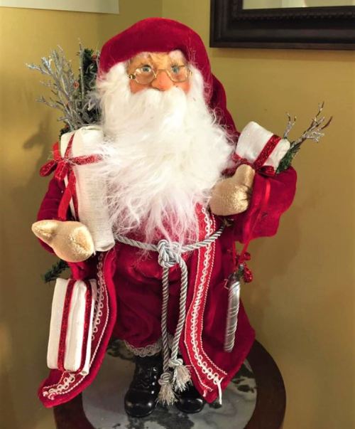 A decorative Santa Claus figure in a red outfit, holding gifts and greenery, standing on a table.