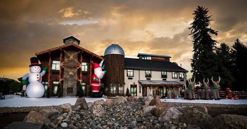 A festive building decorated with large inflatable snowmen, Santa, and reindeer against a dramatic sunset sky.