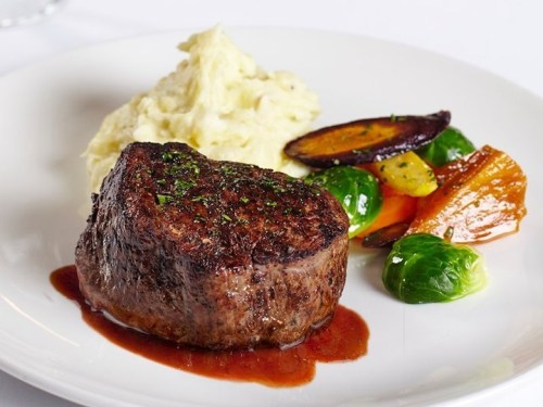 A plated meal featuring a juicy steak, creamy mashed potatoes, and colorful roasted vegetables.
