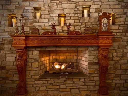 A rustic stone fireplace with a wooden mantel, decorative deer figurines, candles, and a vintage clock.
