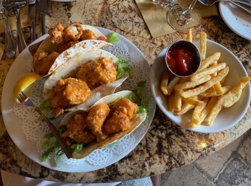 A plate of three spicy shrimp tacos with lettuce and a side of fries and ketchup on a marble table.