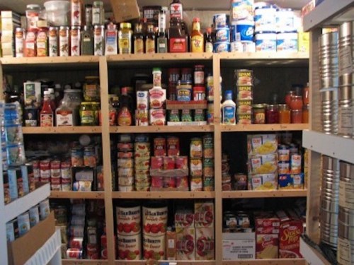 A well-stocked pantry filled with various canned goods, sauces, and condiments on wooden shelves.